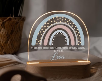 May include: A wooden base with a light-up acrylic rainbow with gold polka dots. The rainbow is in shades of pink and blue. The base has the text "SEI STETS MUTIG, FRÖHLICH, EHRLICH, ANDERS, VERRÜCKT, EINZIGARTIG, BESONDERS SEI DU SELBST" and the name "Leon" in cursive.