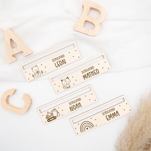 May include: Four wooden name tags with different animal and vehicle illustrations. The tags read "Schulkind Leon", "Schulkind Matteo", "Schulkind Noah", and "Schulkind Emma".