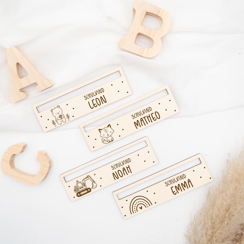 May include: Four wooden name tags with different animal and vehicle illustrations. The tags read "Schulkind Leon", "Schulkind Matteo", "Schulkind Noah", and "Schulkind Emma".