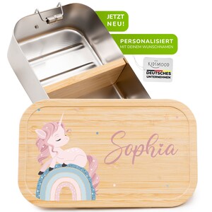 May include: A personalized lunchbox with a wooden lid featuring a pink unicorn with a rainbow and the name "Sophia". The lunchbox is made of stainless steel and has a bamboo divider.