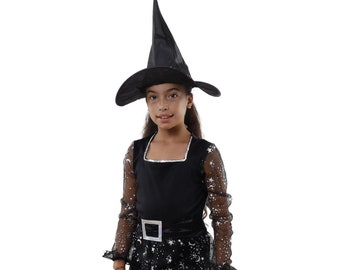 May include: A young girl dressed as a witch for Halloween. She is wearing a black dress with silver stars and moons, a black witch hat, and black shoes.