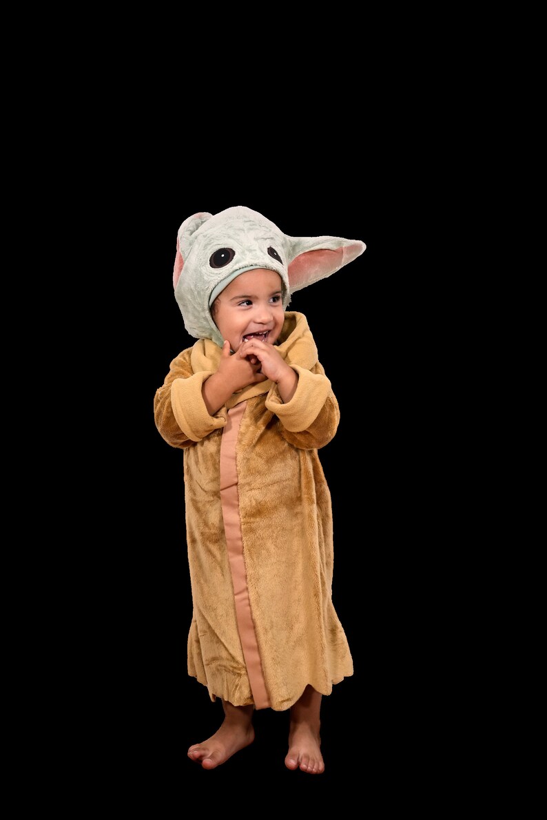 Puede incluir: Un ni&ntilde;o o ni&ntilde;a lleva una bata de felpa marr&oacute;n con una capucha de personaje verde y rosa. El ni&ntilde;o o ni&ntilde;a sonr&iacute;e y mira hacia la derecha.