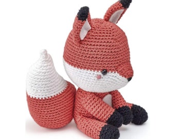 May include: A crocheted fox amigurumi toy with a white belly and a red body. The fox is sitting with its tail curled behind it. The toy has black eyes and a black nose.