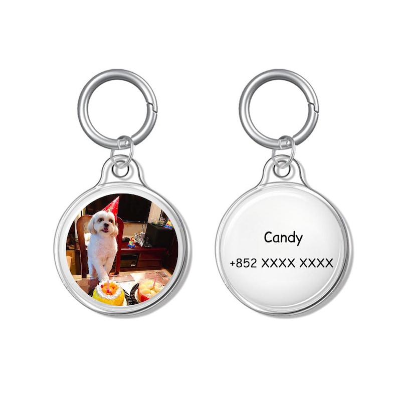 May include: A silver key chain with a clear plastic tag. The tag has a photo of a small white dog wearing a red party hat and a phone number that reads +852 XXXX XXXX. The text "Candy" is printed on the tag.
