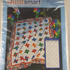 May include: QuiltSmart Pinwheel Spin quilting pattern featuring a colorful pinwheel design with a white background. The pattern includes instructions for making a quilt with no curved piecing. The pattern is by Mary Devendorf.
