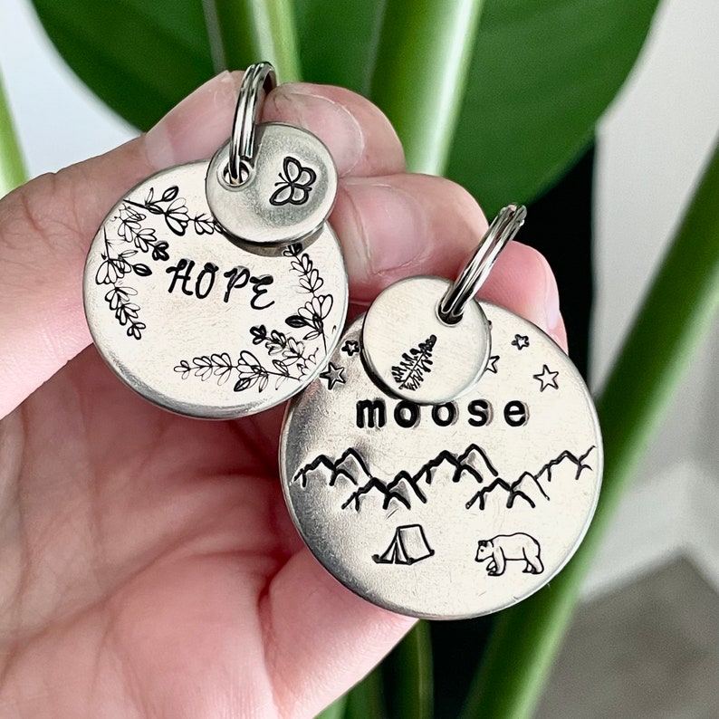 May include: Two silver metal keychains. One keychain has the word "HOPE" surrounded by floral designs and a small butterfly charm. The other keychain has the word "moose" above a mountain range, a tent, and a bear.