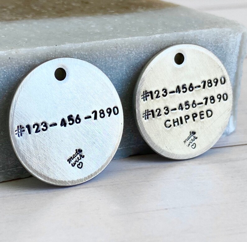 May include: Two silver-colored, circular pet tags with stamped text. One tag displays the phone number #123-456-7890. The other tag has the same number and the word "CHIPPED". Both tags have a small hole at the top and the words "made with" and a heart symbol at the bottom.