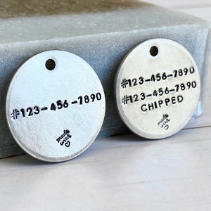 May include: Two silver metal pet tags with stamped text. One tag has the phone number #123-456-7890. The other tag has the same number and the word "CHIPPED". Both tags have a small heart and the words "made with" stamped on them.