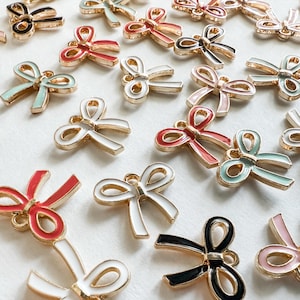 Può includere: Un assortimento di ciondoli a forma di fiocco colorati con bordi dorati. I ciondoli sono in vari colori, tra cui rosso, bianco, nero, rosa e verde acqua. Questi ciondoli decorativi sono ideali per la creazione di gioielli o progetti artigianali.