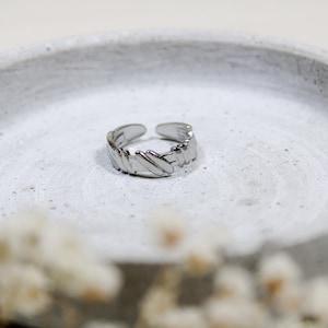 Könnte beinhalten: Ein silberner Ring mit einem strukturierten, geometrischen Design. Der Ring liegt auf einer weißen, strukturierten Oberfläche.