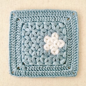 May include: A crocheted square with a blue border and a white star in the centre. The star is made with a granny stitch pattern.