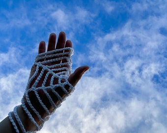 May include: A white crocheted glove with a geometric pattern, against a blue sky with white clouds.
