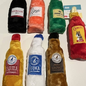 May include: Set of eight plush dog toys shaped like bottles of alcohol. The bottles are labeled with different types of alcohol, including Merlot, Rose, Champagne, Tequila, Vodka, Whiskey, and Hot Sauce. The toys are made by ZippyPaws.