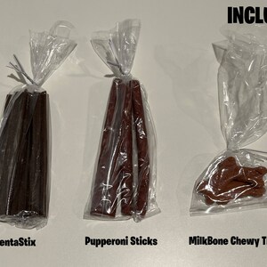 May include: Three bags of dog treats. The first bag contains brown DentaStix, the second bag contains red Pupperoni Sticks, and the third bag contains brown MilkBone Chewy Treats. The text "INCLUDED" is written in black at the top of the image.