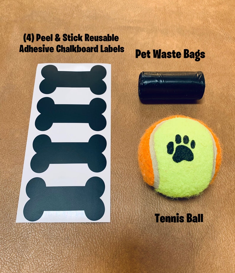 May include: Four black chalkboard bone-shaped labels, a roll of black pet waste bags, and a yellow tennis ball with a black paw print.