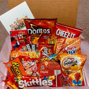 K&ouml;nnte beinhalten: Ein Geschenkkorb gef&uuml;llt mit einer Auswahl an Snacks, darunter Doritos, Cheez-Its, Skittles, Reese's und Goldfish Cracker. Der Korb enth&auml;lt auch eine Schachtel Frosted Flakes M&uuml;sli und eine Gru&szlig;karte. Die Snacks sind auf rosa Seidenpapier angeordnet.