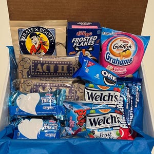 K&ouml;nnte beinhalten: Eine Geschenkbox gef&uuml;llt mit verschiedenen Snacks, darunter Pirate's Booty, Kellogg's Frosted Flakes, Goldfish Grahams, Oreo-Kekse, Rice Krispies Treats und Welch's Fruit Snacks. Die Box ist mit blauem Seidenpapier ausgekleidet.