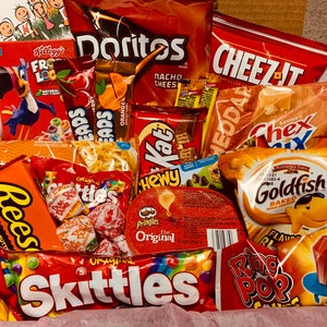 K&ouml;nnte beinhalten: Eine Geschenkbox gef&uuml;llt mit einer Auswahl an Snacks und S&uuml;&szlig;igkeiten. Enth&auml;lt T&uuml;ten mit Doritos, Cheez-Its, Chex Mix, Goldfish-Crackern, Reese's Peanut Butter Cups, Skittles und Ring Pop-Lutschern. Eine Schachtel Froot Loops-Cerealien ist ebenfalls sichtbar.