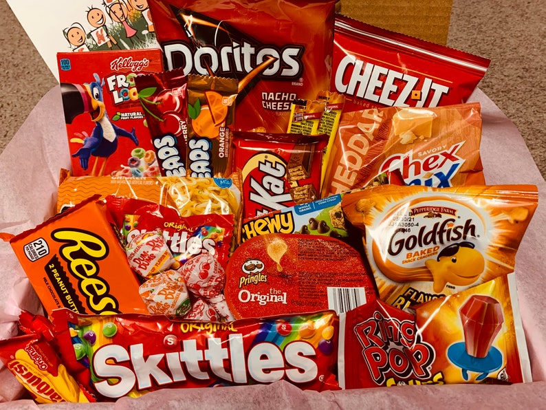 K&ouml;nnte beinhalten: Eine Geschenkbox gef&uuml;llt mit einer Auswahl an Snacks und S&uuml;&szlig;igkeiten. Enth&auml;lt T&uuml;ten mit Doritos, Cheez-Its, Chex Mix, Goldfish-Crackern, Reese's Peanut Butter Cups, Skittles und Ring Pop-Lutschern. Eine Schachtel Froot Loops-Cerealien ist ebenfalls sichtbar.