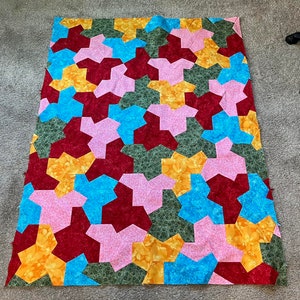 May include: A patchwork quilt with a geometric pattern in shades of pink, red, blue, yellow, and green.
