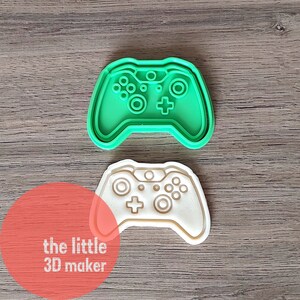 May include: Two plastic cookie cutters shaped like a video game controller. The top cutter is green and the bottom cutter is white.