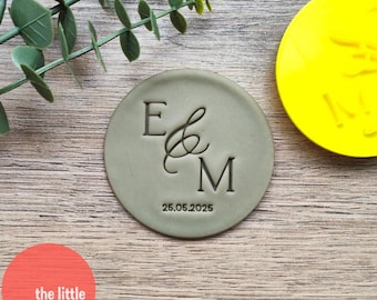 May include: A green round cookie cutter with the letters E & M and the date 25.05.2025.