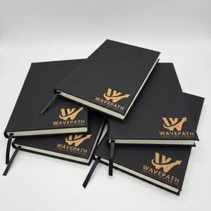 May include: A stack of five black notebooks with a gold logo featuring a stylized letter W and an upward arrow, accompanied by the text "WAVEPATH LOGISTICS & SHIPPING". Each notebook includes a black ribbon bookmark and off-white pages.
