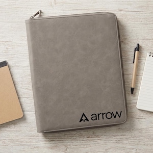 May include: A rectangular gray zippered portfolio case with a smooth, matte texture. The word arrow is printed in black lowercase letters in the bottom right corner, accompanied by a small triangular icon to the left of the text.