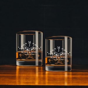 May include: Two clear, personalized whiskey glasses with gold rims, filled with amber liquid and ice cubes. Each glass features the initials "M" and "J" with the names "Mark & Julie" and the date "6-29-2024" etched on the front.