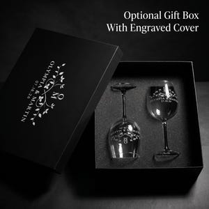 May include: A black gift box with an engraved cover, containing two wine glasses. The glasses and box are personalized with the names "Olympia & Martin" and the date "07.18.26". The box text reads "Optional Gift Box With Engraved Cover".