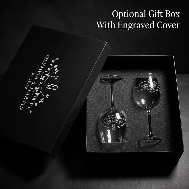 May include: A black gift box with an engraved cover, containing two wine glasses. The glasses and box are personalized with the names "Olympia & Martin" and the date "07.18.26". The box text reads "Optional Gift Box With Engraved Cover".