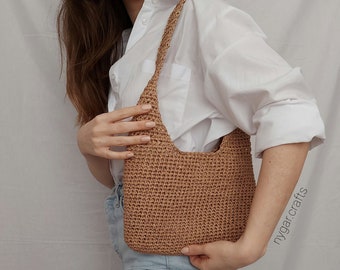 May include: A brown crocheted shoulder bag with a slouchy, crescent shape. The bag is worn by a person wearing a white button-down shirt and blue jeans.