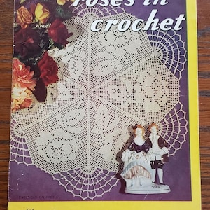 May include: A vintage Lily crochet design book number 71 titled roses in crochet. The cover features a white crocheted doily with a rose pattern, a bouquet of red and yellow roses, and a porcelain figurine of a couple in period attire.