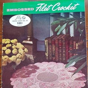 May include: Embossed Filet Crochet design book number 82 by Lily. The cover features a pink crocheted doily on a dark brown surface with a bouquet of yellow flowers and a stack of books in the background. The book costs 10 cents.