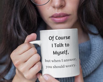 Könnte beinhalten: Weiße Keramik-Tasse mit dem Text "Of Course I Talk to Myself, but when I answer, you should worry." Die Tasse wird von einer Person gehalten, die einen blauen Pullover trägt.