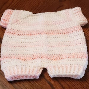 May include: A handmade, crochet baby romper in white with horizontal stripes of soft pink. The romper features short sleeves and leg openings, showcasing a delicate, textured stitch. The garment is designed for a baby.