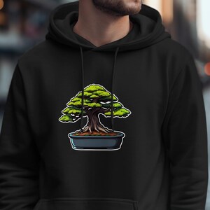Peut inclure: Un sweat à capuche noir arborant une illustration de bonsaï avec un tronc brun foncé et un feuillage vert vif, planté dans un pot en céramique gris foncé. Le sweat-shirt est doté d'une capuche à cordon de serrage et de manches longues noires.