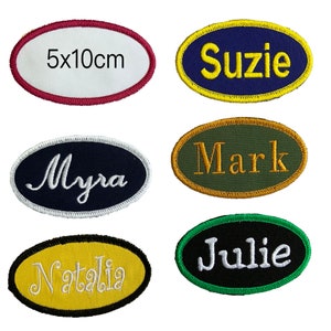 May include: Six oval-shaped embroidered iron-on patches with white lettering on different coloured backgrounds. The patches read "5x10cm", "Suzie", "Myra", "Mark", "Julie", and "Natalia".