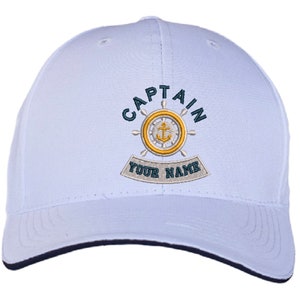 May include: White baseball cap with blue and yellow embroidery. The embroidery says "CAPTAIN" with a nautical wheel and anchor design. The text "YOUR NAME" is below the wheel.