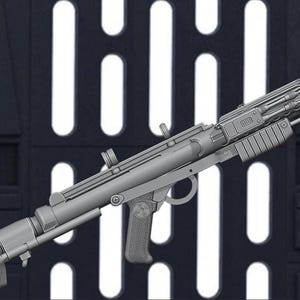 May include: A gray blaster rifle prop, a replica of a weapon from a science fiction film. The prop gun has a detailed design with various attachments and a textured grip. The background features a dark panel with white rectangular cutouts.