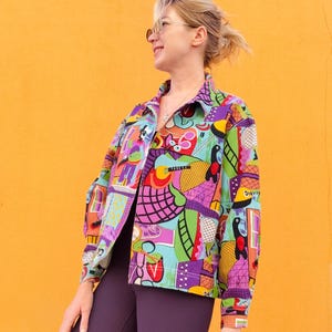 May include: A colorful button-up jacket with a vibrant, abstract pattern in shades of purple, green, blue, and red. The jacket features a collared neckline and long sleeves. The background is a solid orange.