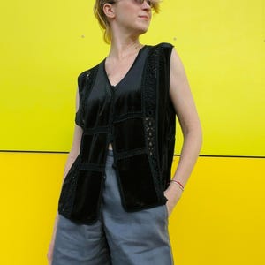 May include: A black velvet vest with crocheted detailing and a button closure. The vest is worn over a pair of gray shorts.