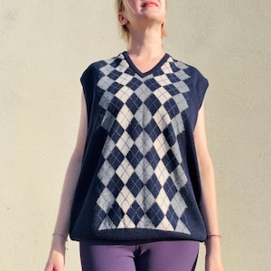 Puede incluir: Un chaleco de punto azul marino con diseño de rombos. El patrón presenta rombos blancos y azul claro. El chaleco se combina con leggings morados. La persona de la imagen lleva gafas de sol.