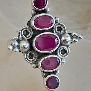 Könnte beinhalten: Ein silberner Ring mit einem rautenförmigen Design, das mit fünf rosafarbenen ovalen Edelsteinen besetzt ist.