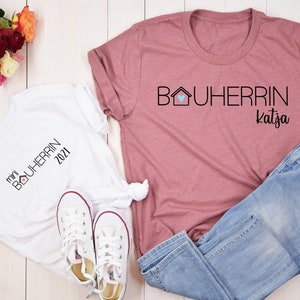 Könnte beinhalten: Zwei weiße T-Shirts mit schwarzem Text und einer Hausgrafik. Der Text auf einem Shirt lautet "mini BOUHERRIN 2021". Der Text auf dem anderen Shirt lautet "BOUHERRIN katja".