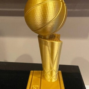 May include: A gold-colored basketball trophy with a basketball on top. The base of the trophy has the NBA logo and the text "Larry O'Brien Championship Trophy".