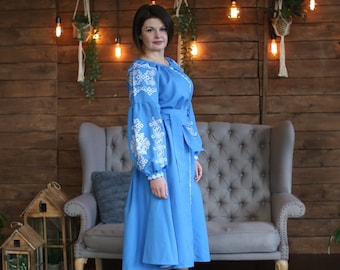 Könnte beinhalten: Ein leuchtend blaues Midikleid mit langen, voluminösen Ärmeln, die mit aufwendigen weißen geometrischen Stickereien verziert sind. Das Kleid verfügt über einen passenden Stoffgürtel in der Taille, einen Rundhalsausschnitt und einen ausgestellten Rock.