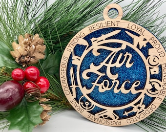 May include: A wooden Christmas ornament with a blue glitter background and the words "Air Force" in a white script font. The ornament is surrounded by a circle of words including "strong", "courageous", "brave", "passionate", "dedicated", "honorable", "proud", "loyal", and "resilient".