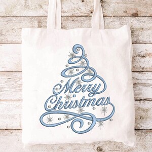 May include: A white tote bag with a blue embroidered Christmas tree design and the words "Merry Christmas". The design includes snowflakes and small silver beads. The bag has two white handles.