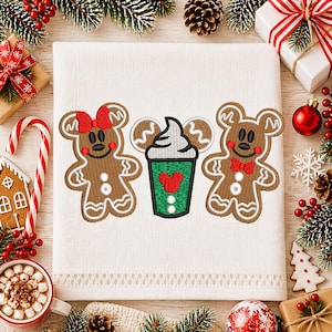 Puede incluir: Toalla blanca bordada con dos figuras de pan de jengibre con orejas de Mickey Mouse y una taza verde con un corazón rojo. Las figuras de pan de jengibre tienen lazos rojos. Tema festivo.